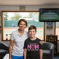 Woman and young boy standing together in a room with a tennis court visible through a window.  The boy is wearing a Cows Corner T-shirt with the funny and sweet tennis slogan on the front that reads 'Tennis with Mums. Best. Day. Ever!'  Cows Corner gifts are perfect for sport-mad fans, these gifts work brilliantly for birthdays, new baby celebrations, Father’s Day, Mother’s Day, Christmas, anniversaries, thank you gifts, end-of-season team awards, graduations, retirements, and just-because moments