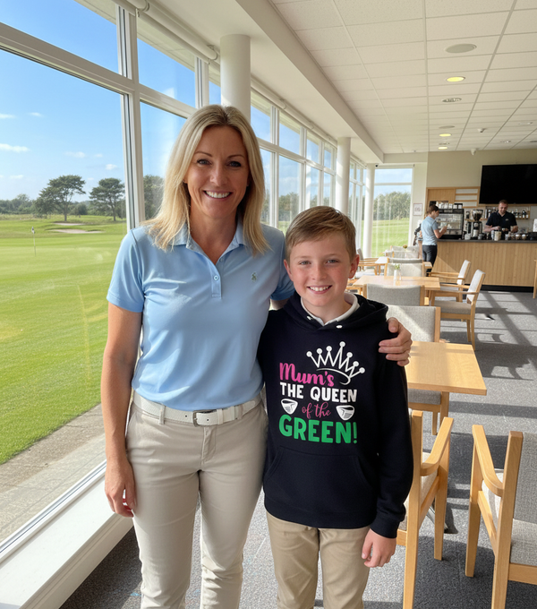 Woman and young boy standing together in a modern indoor setting with large windows showing greenery outside. The boy is wearing a Cows Corner hoodie with a funny golf slogan 'Mum’s the Queen of the Green'. Cows Corner gifts are perfect for sport-mad fans, these gifts work brilliantly for birthdays, new baby celebrations, Father’s Day, Mother’s Day, Christmas, anniversaries, thank you gifts, end-of-season team awards, graduations, retirements, and just-because moments when you want to raise a smile. 
