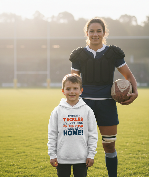 Woman in sports gear holding a rugby ball and a child in a hoodie on a grassy field.  The lady is wearing a Cows Corner hoodie with the funny rugby slogan 'My Mum Tackles Everything on the Pitch and at Home!'. Cows Corner gifts are perfect for sport-mad fans, these gifts work brilliantly for birthdays, new baby celebrations, Father’s Day, Mother’s Day, Christmas, anniversaries, thank you gifts, end-of-season team awards, graduations, retirements, and just-because moments when you want to raise a smile. 
