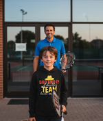 Man and boy holding tennis rackets in front of a building with glass doors. The boy is wearing a Cows Corner hoodie with the funny tennis slogan 'Dad and I? A Doubles Team Built on Love'. Cows Corner gifts are perfect for sport-mad fans, these gifts work brilliantly for birthdays, new baby celebrations, Father’s Day, Mother’s Day, Christmas, anniversaries, thank you gifts, end-of-season team awards, graduations, retirements, and just-because moments when you want to raise a smile. 
