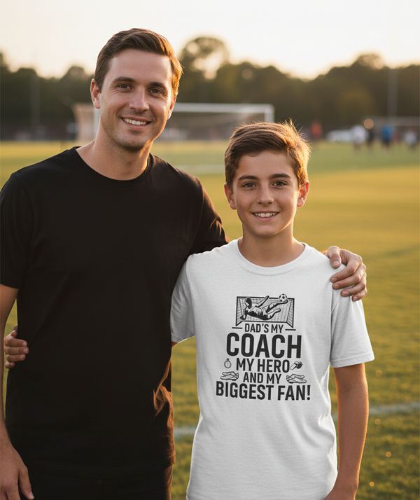 Man and young boy standing on a sports field, with the boy wearing a t-shirt about his father. The boy is wearing a Cows Corner t-shirt with the funny football slogan 'Dad’s My Coach My Hero and My Biggest Fan!'. Cows Corner gifts are perfect for sport-mad fans, these gifts work brilliantly for birthdays, new baby celebrations, Father’s Day, Mother’s Day, Christmas, anniversaries, thank you gifts, end-of-season team awards, graduations, retirements, and just-because moments when you want to raise a smile. 
