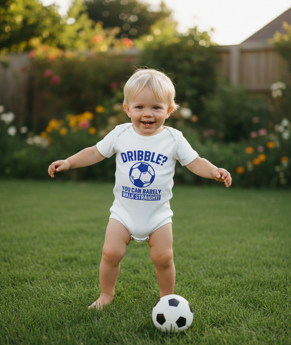 Child wearing a 'Dribble?' onesie playing with a soccer ball in a garden. The baby is wearing a Cows Corner baby grow with a funny football slogan 'Dribble You Can Barely Walk Straight!'. Cows Corner gifts are perfect for sport-mad fans, these gifts work brilliantly for birthdays, new baby celebrations, Father’s Day, Mother’s Day, Christmas, anniversaries, thank you gifts, end-of-season team awards, graduations, retirements, and just-because moments when you want to raise a smile. 

