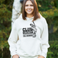 A lady wearing a white hoodie with Funny Cricket Hoodie – 'Club Cricket: Where Everyone’s an All-Rounder' on the front. A Funny Cricket Hoodie, Premium Fabric, Multiple Adult Sizes
