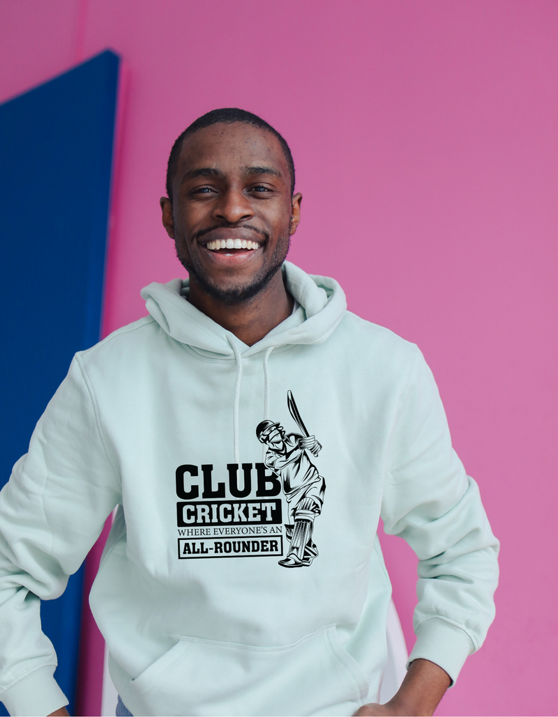 A man wearing a white hoodie with Funny Cricket Hoodie – 'Club Cricket: Where Everyone’s an All-Rounder' on the front. A Funny Cricket Hoodie, Premium Fabric, Multiple Adult Sizes