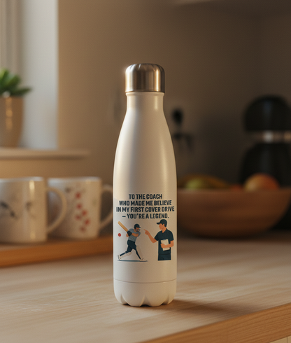 White water bottle with a motivational quote and graphic on a wooden table. This is a Cows Corner water bottle with a funny cricket slogan 'To My Coach Who Made Me Believe in My First Cover Drive – You’re a Legend'. Cows Corner gifts are perfect for sport-mad fans, these gifts work brilliantly for birthdays, new baby celebrations, Father’s Day, Mother’s Day, Christmas, anniversaries, thank you gifts, end-of-season team awards, graduations, retirements, and just-because moments when you want to raise a smile