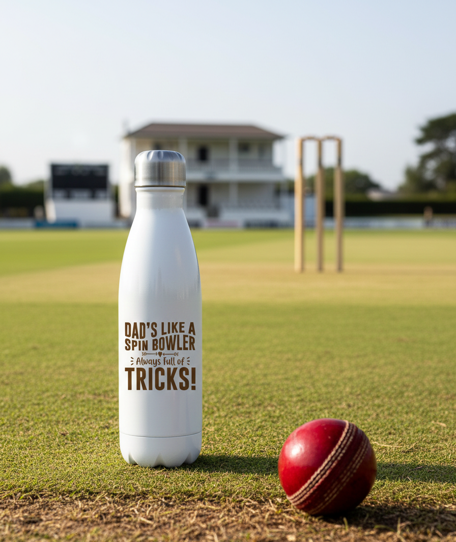 White water bottle with text on a cricket field, next to a red cricket ball. This is a Cows Corner my with a funny cricket slogan 'Dad’s Like a Spin Bowler, Always Full of Tricks!'. Cows Corner gifts are perfect for sport-mad fans, these gifts work brilliantly for birthdays, new baby celebrations, Father’s Day, Mother’s Day, Christmas, anniversaries, thank you gifts, end-of-season team awards, graduations, retirements, and just-because moments when you want to raise a smile. 
