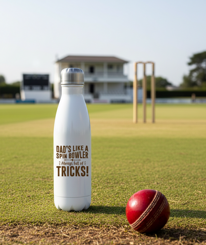 White water bottle with text on a cricket field, next to a red cricket ball. This is a Cows Corner my with a funny cricket slogan 'Dad’s Like a Spin Bowler, Always Full of Tricks!'. Cows Corner gifts are perfect for sport-mad fans, these gifts work brilliantly for birthdays, new baby celebrations, Father’s Day, Mother’s Day, Christmas, anniversaries, thank you gifts, end-of-season team awards, graduations, retirements, and just-because moments when you want to raise a smile. 
