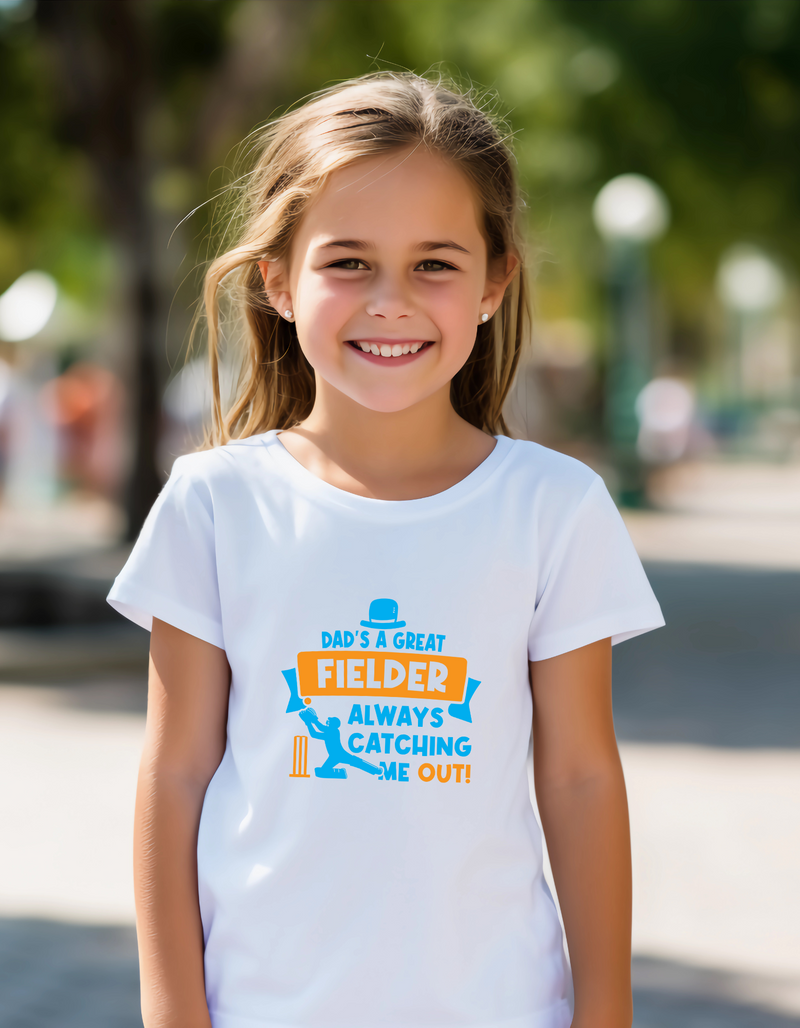 A little girl wearing a Funny Kids Cricket T-Shirt with “Dad Is a Great Fielder, Always Catching Me Out” on the front. Premium Fabric, Multiple Junior Sizes, Perfect for Boys and Girls