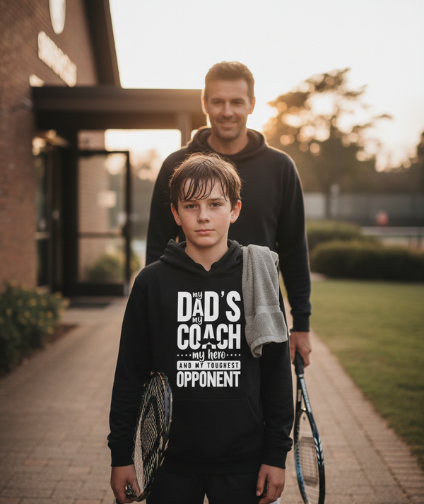 Two people walking outdoors with tennis rackets, one wearing a hoodie with text. The boy is wearing a Cows Corner hoodie with a funny tennis slogan 'My Dads My Coach, My Hero And My Toughest Opponent'. Cows Corner gifts are perfect for sport-mad fans, these gifts work brilliantly for birthdays, new baby celebrations, Father’s Day, Mother’s Day, Christmas, anniversaries, thank you gifts, end-of-season team awards, graduations, retirements, and just-because moments when you want to raise a smile. 
