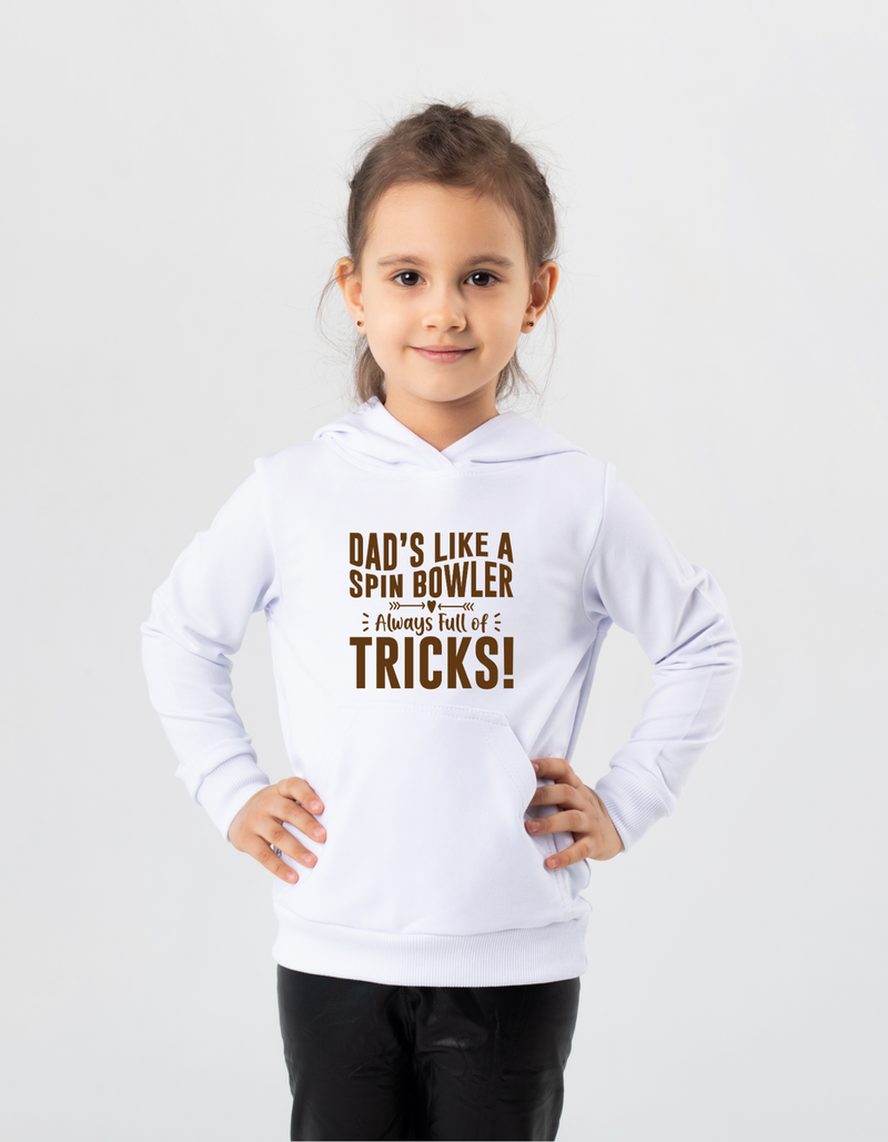 A little girl wearing a white hoodie with Dad’s Like a Spin Bowler, Always Full of Tricks on the front.  A Funny Cricket Hoodie, Premium Fabric, Multiple Junior Sizes, Perfect for Boys and Girls