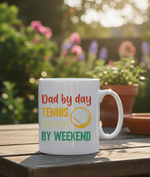 White mug with colorful text and a tennis ball graphic on a wooden table with a garden background. This is a Cows Corner mug with a funny tennis slogan 'Dad By Day, Tennis Champ By Weekend'. Cows Corner gifts are perfect for sport-mad fans, these gifts work brilliantly for birthdays, new baby celebrations, Father’s Day, Mother’s Day, Christmas, anniversaries, thank you gifts, end-of-season team awards, graduations, retirements, and just-because moments when you want to raise a smile. 
