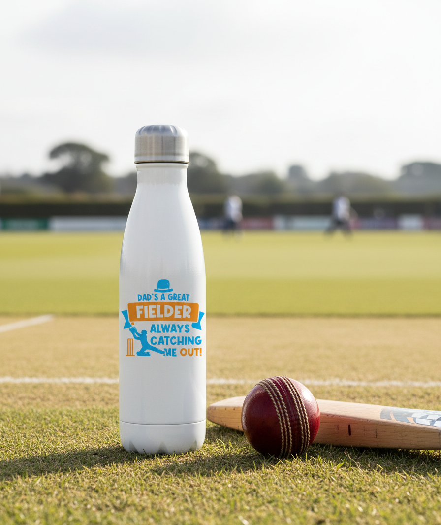 White water bottle with a colorful label on a cricket field. This is a Cows Corner water bottle that has the funny cricket slogan 'Dad is a Great Fielder, Always Catching Me Out'.  Cows Corner gifts are perfect for sport-mad fans, these gifts work brilliantly for birthdays, new baby celebrations, Father’s Day, Mother’s Day, Christmas, anniversaries, thank you gifts, end-of-season team awards, graduations, retirements, and just-because moments when you want to raise a smile. 
