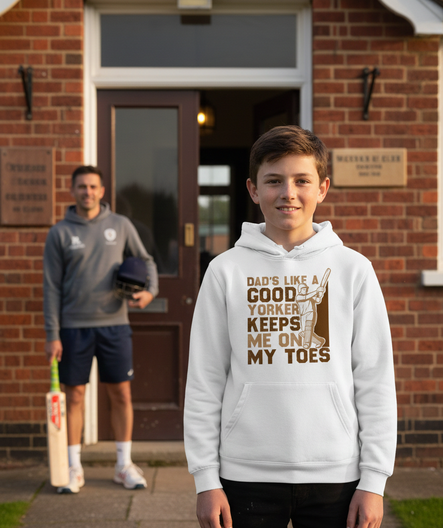 Two boys standing outside a brick building, one wearing a white hoodie with a humorous message. The boy is wearing a Cows Corner hoodie with the funny cricket slogan 'Dads Like A Good Yorker, Keeps Me On My Toes'. Cows Corner gifts are perfect for sport-mad fans, these gifts work brilliantly for birthdays, new baby celebrations, Father’s Day, Mother’s Day, Christmas, anniversaries, thank you gifts, end-of-season team awards, graduations, retirements, and just-because moments when you want to raise a smile. 