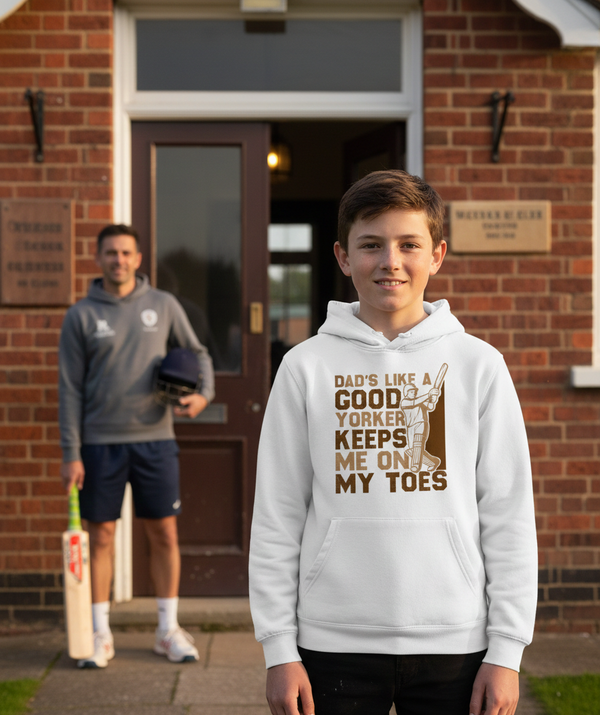 Two boys standing outside a brick building, one wearing a white hoodie with a humorous message. The boy is wearing a Cows Corner hoodie with the funny cricket slogan 'Dads Like A Good Yorker, Keeps Me On My Toes'. Cows Corner gifts are perfect for sport-mad fans, these gifts work brilliantly for birthdays, new baby celebrations, Father’s Day, Mother’s Day, Christmas, anniversaries, thank you gifts, end-of-season team awards, graduations, retirements, and just-because moments when you want to raise a smile. 