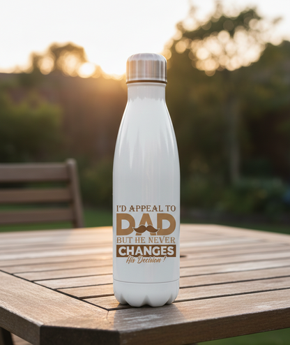 White water bottle with a humorous message on a wooden table outdoors. This is a Cows Corner water bottle with a funny cricket slogan 'I'd Appeal to Dad, But He Never Changes His Decision'. Cows Corner gifts are perfect for sport-mad fans, these gifts work brilliantly for birthdays, new baby celebrations, Father’s Day, Mother’s Day, Christmas, anniversaries, thank you gifts, end-of-season team awards, graduations, retirements, and just-because moments when you want to raise a smile. 
