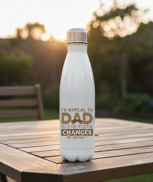 White water bottle with a humorous message on a wooden table outdoors. This is a Cows Corner water bottle with a funny cricket slogan 'I'd Appeal to Dad, But He Never Changes His Decision'. Cows Corner gifts are perfect for sport-mad fans, these gifts work brilliantly for birthdays, new baby celebrations, Father’s Day, Mother’s Day, Christmas, anniversaries, thank you gifts, end-of-season team awards, graduations, retirements, and just-because moments when you want to raise a smile. 
