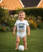 Child wearing a onesie with a rugby-themed message on a grassy area.  The baby is wearing a Cows Corner baby grow with a funny rugby slogan 'My Dad Plays Rugby. What’s Your Superpower?'. Cows Corner gifts are perfect for sport-mad fans, these gifts work brilliantly for birthdays, new baby celebrations, Father’s Day, Mother’s Day, Christmas, anniversaries, thank you gifts, end-of-season team awards, graduations, retirements, and just-because moments when you want to raise a smile. 
