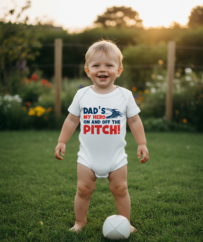 Child wearing a onesie with a humorous message about a dad, standing on grass with a soccer ball. The baby is wearing a Cows Corner baby grow with a funny rugby slogan 'Dad’s My Hero on and off the Pitch!'.  Cows Corner gifts are perfect for sport-mad fans, these gifts work brilliantly for birthdays, new baby celebrations, Father’s Day, Mother’s Day, Christmas, anniversaries, thank you gifts, end-of-season team awards, graduations, retirements, and just-because moments when you want to raise a smile. 
