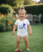 Child wearing a white onesie with blue text and graphics, standing on grass with a garden background. The baby is wearing a Cows Corner baby grow with a funny cricket slogan 'Dad Bowled Me Over With His Dad Jokes'. Cows Corner gifts are perfect for sport-mad fans, these gifts work brilliantly for birthdays, new baby celebrations, Father’s Day, Mother’s Day, Christmas, anniversaries, thank you gifts, end-of-season team awards, graduations, retirements, and just-because moments when you want to raise a smile.