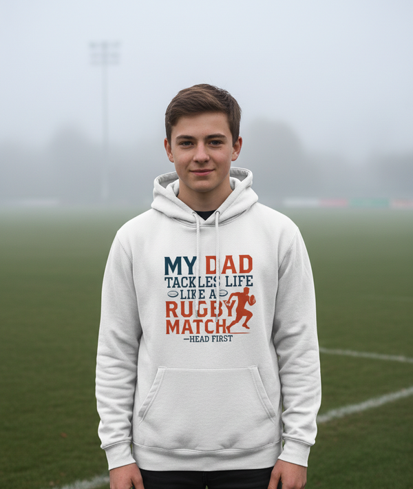 Person wearing a hoodie with a humorous quote on a sports field. A Cows Corner hoodie with slogan 'My Dad Tackles Life Like a Rugby Match- Head First'.  Cows Corner gifts are perfect for sport-mad fans, these gifts work brilliantly for birthdays, new baby celebrations, Father’s Day, Mother’s Day, Christmas, anniversaries, thank you gifts, end-of-season team awards, graduations, retirements, and just-because moments when you want to raise a smile. 
