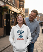 Woman wearing a hoodie with a humorous graphic and text, standing next to a man on a street. The girl is wearing a Cows Corner hoodie with the funny darts slogan 'I Love My Dad… Even If He Can’t Hit A Double'. Cows Corner gifts are perfect for sport-mad fans, these gifts work brilliantly for birthdays, new baby celebrations, Father’s Day, Mother’s Day, Christmas, anniversaries, thank you gifts, end-of-season team awards, graduations, retirements, and just-because moments when you want to raise a smile. 
