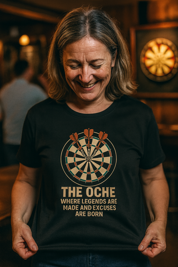 Woman wearing a black t-shirt with a dartboard design and text in a pub setting with a Cows Corner slogan The oche where legends are made and excuses are born.