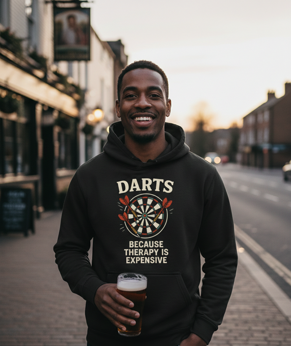 Man wearing a hoodie with a dartboard design and text, standing on a street. The man is wearing a Cows Corner hoodie with the funny darts slogan 'Darts Because Therapy is Expensive '. Cows Corner gifts are perfect for sport-mad fans, these gifts work brilliantly for birthdays, new baby celebrations, Father’s Day, Mother’s Day, Christmas, anniversaries, thank you gifts, end-of-season team awards, graduations, retirements, and just-because moments when you want to raise a smile. 
