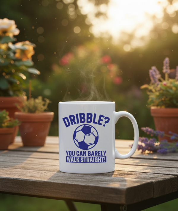 White mug with blue text and soccer graphic on a wooden table outdoors. This is a Cows Corner mug with a funny football slogan 'Dribble You Can Barely Walk Straight!'. Cows Corner gifts are perfect for sport-mad fans, these gifts work brilliantly for birthdays, new baby celebrations, Father’s Day, Mother’s Day, Christmas, anniversaries, thank you gifts, end-of-season team awards, graduations, retirements, and just-because moments when you want to raise a smile. 
