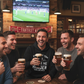 Group of men enjoying Guinness beer in a pub with a sports event on TV with one wearing a Cows Corner funny slogan hoodie