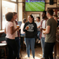 Group of people in a pub watching a sports match on television wearing a Cows Corner funny slogan hoodie