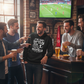 Group of men in a bar watching sports on TV and drinking beer wearing a Cows Corner funny slogan hoodie