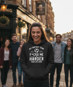 Person wearing a black hoodie with humorous text on a city street. The lady is wearing a Cows Corner hoodie with the funny football slogan 'My Fantasy Team F*cks Me Harder Than Life Does'. Cows Corner gifts are perfect for sport-mad fans, these gifts work brilliantly for birthdays, new baby celebrations, Father’s Day, Mother’s Day, Christmas, anniversaries, thank you gifts, end-of-season team awards, graduations, retirements, and just-because moments when you want to raise a smile. 
