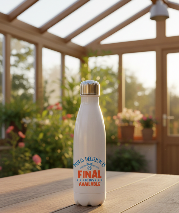 White insulated bottle with a gold cap on a wooden surface in a sunroom with plants and flowers. This is a Cows Corner water bottle with a funny cricket slogan 'Mum’s Decision is Final – No DRS Available.'. Cows Corner gifts are perfect for sport-mad fans, these gifts work brilliantly for birthdays, new baby celebrations, Father’s Day, Mother’s Day, Christmas, anniversaries, thank you gifts, end-of-season team awards, graduations, retirements, and just-because moments when you want to raise a smile. 
