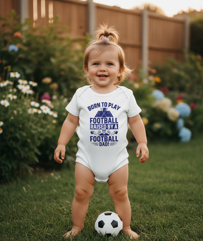 Child wearing a onesie with a football-themed message, standing in a garden with a soccer ball. The baby is wearing a Cows Corner baby grow with a funny football slogan 'Born To Play Football. Raised by a Football Dad!'. Cows Corner gifts are perfect for sport-mad fans, these gifts work brilliantly for birthdays, new baby celebrations, Father’s Day, Mother’s Day, Christmas, anniversaries, thank you gifts, end-of-season team awards, graduations, retirements, and just-because moments