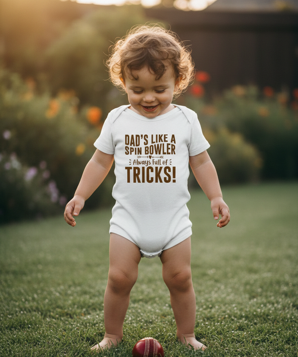 Child wearing a onesie with humorous text outdoors. The baby is wearing a Cows Corner baby grow with a funny cricket slogan 'Dad’s Like a Spin Bowler, Always Full of Tricks!'. Cows Corner gifts are perfect for sport-mad fans, these gifts work brilliantly for birthdays, new baby celebrations, Father’s Day, Mother’s Day, Christmas, anniversaries, thank you gifts, end-of-season team awards, graduations, retirements, and just-because moments when you want to raise a smile. 

