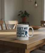 Mug with text on a wooden table in a room with chairs and a plant. This is a Cows Corner mug with a funny football slogan 'I Get My Tekkers From Dad'. Cows Corner gifts are perfect for sport-mad fans, these gifts work brilliantly for birthdays, new baby celebrations, Father’s Day, Mother’s Day, Christmas, anniversaries, thank you gifts, end-of-season team awards, graduations, retirements, and just-because moments when you want to raise a smile. 
