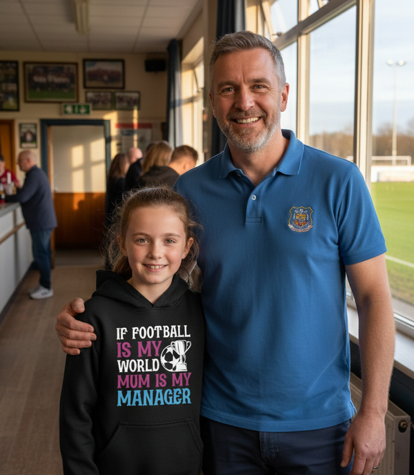 Man and young girl standing together in a sports facility, with the man wearing a blue polo shirt and the girl in a black hoodie. The girl is wearing a Cows Corner hoodie with a funny football slogan 'If Football Is My World Mum Is My Manager'.  Cows Corner gifts are perfect for sport-mad fans, these gifts work brilliantly for birthdays, new baby celebrations, Father’s Day, Mother’s Day, Christmas, anniversaries, thank you gifts, end-of-season team awards, graduations, retirements, and just-because moments 
