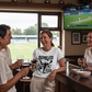People in a pub watching cricket on TV, one person wearing a Cows Corner T-shirt with the funny cricket slogan on the front that reads 'BOWLED Over by Love' shirt. Cows Corner gifts are perfect for sport-mad fans, these gifts work brilliantly for birthdays, new baby celebrations, Father’s Day, Mother’s Day, Christmas, anniversaries, thank you gifts, end-of-season team awards, graduations, retirements, and just-because moments when you want to raise a smile. 