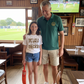Man and young girl standing together in a pub with a TV showing cricket in the background.  The young girl is wearing a Cows Corner t-shirt with the funny and sweet cricket slogan on the front that reads 'Dad’s Like a Spin Bowler, Always Full of Tricks!'