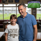 Man and young girl standing together in a sports bar with a TV showing a football game.  The girl is wearing a Cows Corner T-shirt with the funny and sweet football slogan on the front that reads 'Dad’s First Love: Football. Dad’s Second Love: Me'.  Cows Corner gifts are perfect for sport-mad fans, these gifts work brilliantly for birthdays, new baby celebrations, Father’s Day, Mother’s Day, Christmas, anniversaries, thank you gifts, end-of-season team awards, graduations, retirements, and just-because