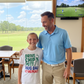 Man and young girl standing together in a room with a golf simulator in the background. The girl is wearing a Cows Corner t-shirt with the funny and sweet golf saying on the front that reads 'Drive Chip Putt Hug Dad Repeat!'  Cows Corner gifts are perfect for sport-mad fans, these gifts work brilliantly for birthdays, new baby celebrations, Father’s Day, Mother’s Day, Christmas, anniversaries, thank you gifts, end-of-season team awards, graduations, retirements, and just-because moments 