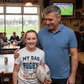 Man and young girl holding a rugby ball in a pub setting with rugby match on TV. The girl is wearing a Cows Corner t-shirt with the funny and sweet rugby slogan on the front that reads 'My Dad Plays Rugby. What’s Your Superpower?'.Cows Corner gifts are perfect for sport-mad fans, these gifts work brilliantly for birthdays, new baby celebrations, Father’s Day, Mother’s Day, Christmas, anniversaries, thank you gifts, end-of-season team awards, graduations, retirements, and just-because moments 