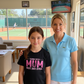 Woman and young girl standing together in a room with a tennis court view.  The girl is wearing a Cows Corner T-shirt with the funny and sweet tennis slogan on the front that reads 'Tennis with Mums. Best. Day. Ever!'.  Cows Corner gifts are perfect for sport-mad fans, these gifts work brilliantly for birthdays, new baby celebrations, Father’s Day, Mother’s Day, Christmas, anniversaries, thank you gifts, end-of-season team awards, graduations, retirements, and just-because moments 