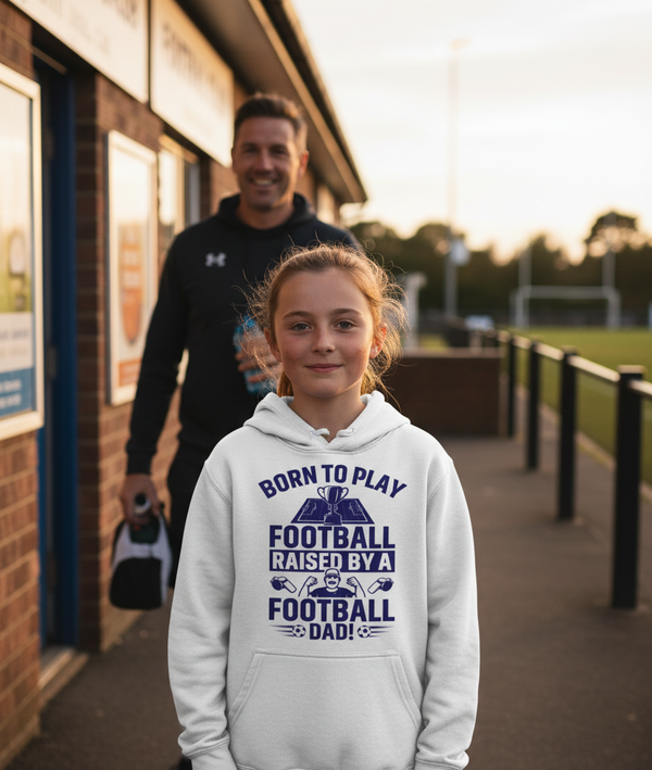 Girl wearing a hoodie with text about playing football and being raised by a football dad, standing in front of a building. The girl is wearing a Cows Corner hoodie with a funny football slogan 'Born To Play Football. Raised by a Football Dad!'. Cows Corner gifts are perfect for sport-mad fans, these gifts work brilliantly for birthdays, new baby celebrations, Father’s Day, Mother’s Day, Christmas, anniversaries, thank you gifts, end-of-season team awards, graduations, retirements, and just-because moments 