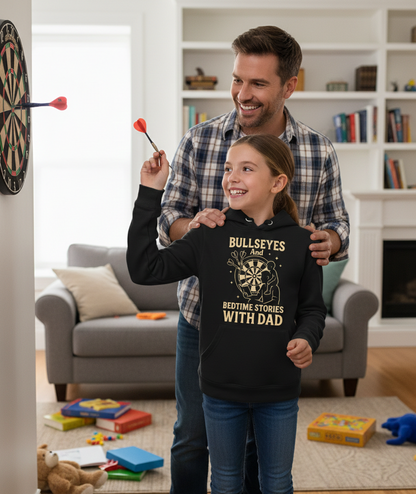 Man and young girl playing darts together in a living room.  The young girl is wearing a Cows Corner hoodie with the funny darts slogan that reads 'Bullseyes And Bedtime Stories With Dad'.  Cows Corner gifts are perfect for sport-mad fans, these gifts work brilliantly for birthdays, new baby celebrations, Father’s Day, Mother’s Day, Christmas, anniversaries, thank you gifts, end-of-season team awards, graduations, retirements, and just-because moments when you want to raise a smile. 
