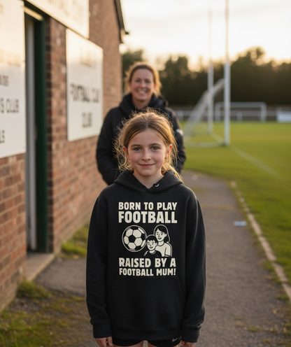 Girl wearing a black hoodie with football-themed text on a sports field. The girl is wearing a Cows Corner hoodie with a funny football slogan 'Born To Play Football Raised by a Football Mum!'. Cows Corner gifts are perfect for sport-mad fans, these gifts work brilliantly for birthdays, new baby celebrations, Father’s Day, Mother’s Day, Christmas, anniversaries, thank you gifts, end-of-season team awards, graduations, retirements, and just-because moments when you want to raise a smile. 
