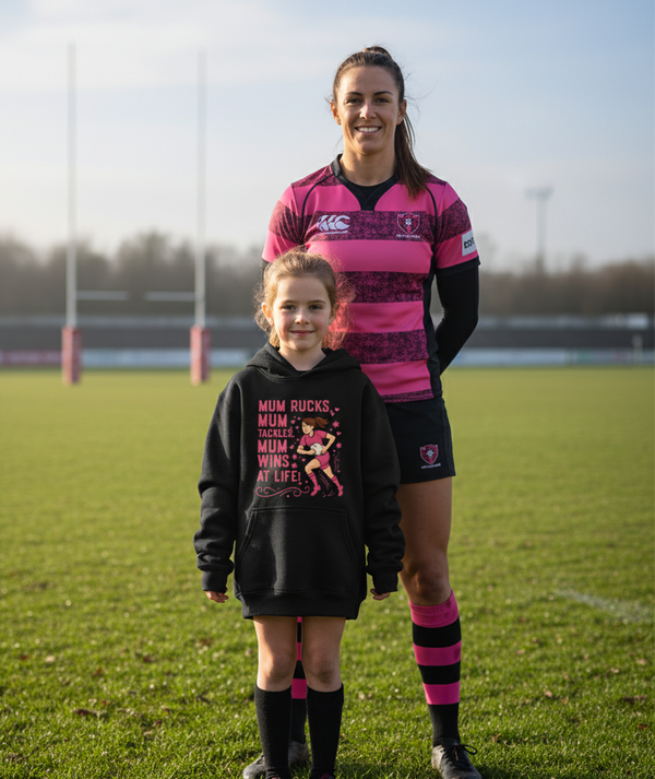 Woman and child on a rugby field wearing pink and black sports outfits. The girl is wearing a Cows Corner hoodie with the funny rugby slogan 'Mum Rucks, Mum Tackles, Mum Wins at Life!'. Cows Corner gifts are perfect for sport-mad fans, these gifts work brilliantly for birthdays, new baby celebrations, Father’s Day, Mother’s Day, Christmas, anniversaries, thank you gifts, end-of-season team awards, graduations, retirements, and just-because moments when you want to raise a smile. 
