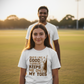 Two people standing on a grassy field with a girl wearing a t-shirt with a humorous graphic and text. The girl is wearing a Cows Corner t-shirt with the funny cricket slogan 'Dads Like A Good Yorker, Keeps Me On My Toes'. Cows Corner gifts are perfect for sport-mad fans, these gifts work brilliantly for birthdays, new baby celebrations, Father’s Day, Mother’s Day, Christmas, anniversaries, thank you gifts, end-of-season team awards, graduations, retirements, and just-because moments 