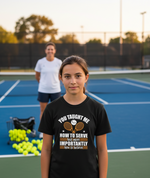 Girl wearing a black t-shirt on a tennis court with another person in the background. The girl is wearing a Cows Corner t-shirt with the funny tennis slogan 'You Taught Me How To Serve but More Importantly How To Believe'. Cows Corner gifts are perfect for sport-mad fans, these gifts work brilliantly for birthdays, new baby celebrations, Father’s Day, Mother’s Day, Christmas, anniversaries, thank you gifts, end-of-season team awards, graduations, retirements, and just-because moments when you want to raise 