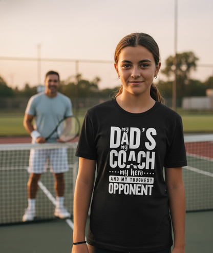 Girl wearing a black t-shirt with text on a tennis court, with a man in the background holding a tennis racket. The girl is wearing a Cows Corner t-shirt with the funny tennis slogan 'My Dads My Coach, My Hero And My Toughest Opponent'. Cows Corner gifts are perfect for sport-mad fans, these gifts work brilliantly for birthdays, new baby celebrations, Father’s Day, Mother’s Day, Christmas, anniversaries, thank you gifts, end-of-season team awards, graduations, retirements, and just-because moments 